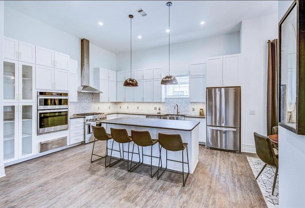 12001 Inwood Road, Unit 3501 Dallas, TX 75244 - Photo 7 of 15 Kitchen featuring a center island, decorative light fixtures, wall chimney range hood, stainless steel appliances, and tasteful backsplash