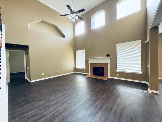 an empty room with wooden floor a fireplace a ceiling fan and windows