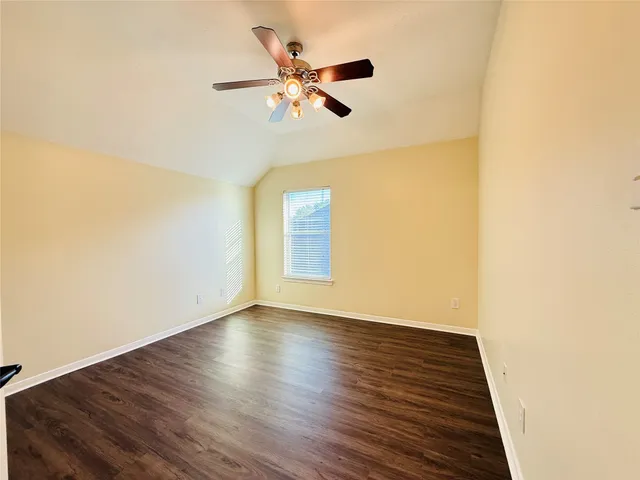 a view of an empty room with wooden floor and a ceiling fan