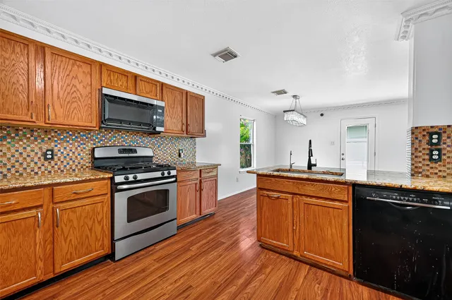 a kitchen with stainless steel appliances granite countertop wooden cabinets a stove top oven a sink and dishwasher with wooden floor