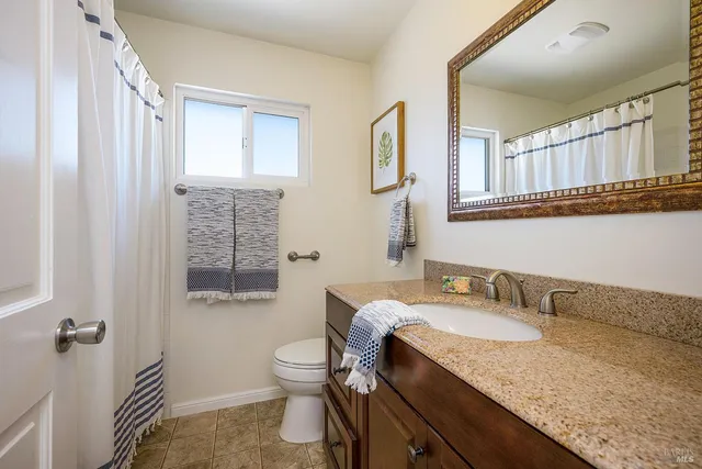 a bathroom with a granite countertop sink a toilet a mirror and a tub