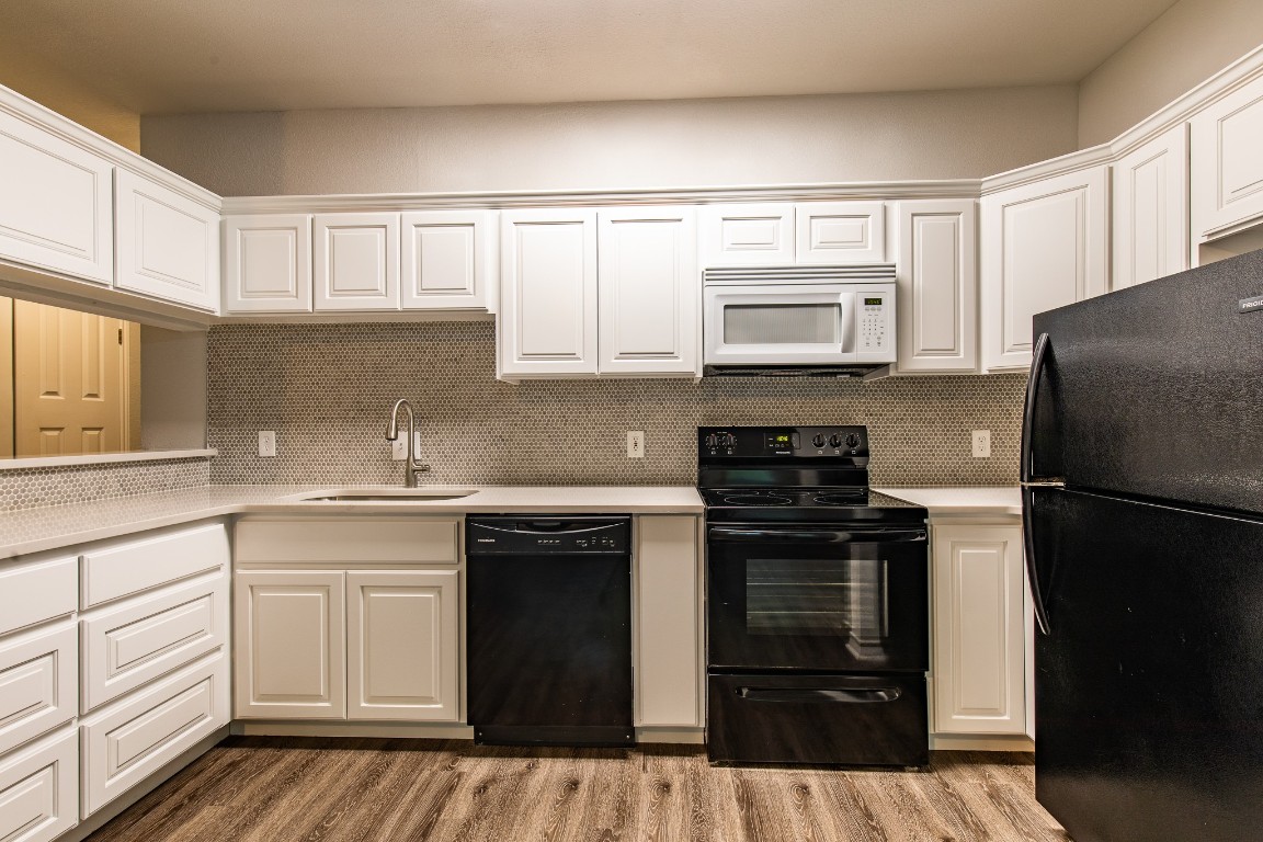 2204 San Gabriel Street, Unit 104 Austin, TX 78705 - Photo 3 of 18 Kitchen with black appliances, light countertops, light wood finished floors, white cabinets, and decorative backsplash