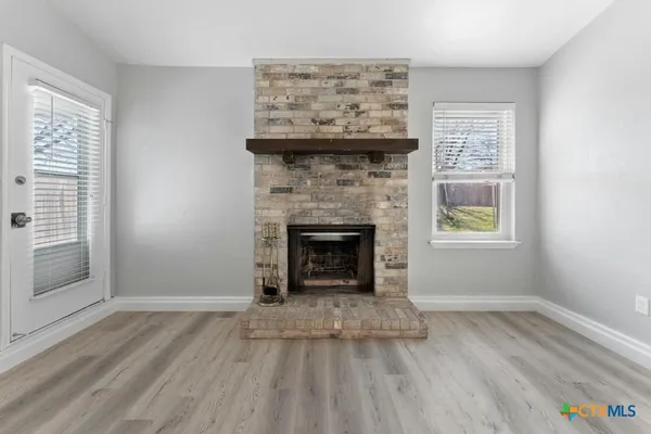 a view of an empty room with wooden floor fireplace and a window