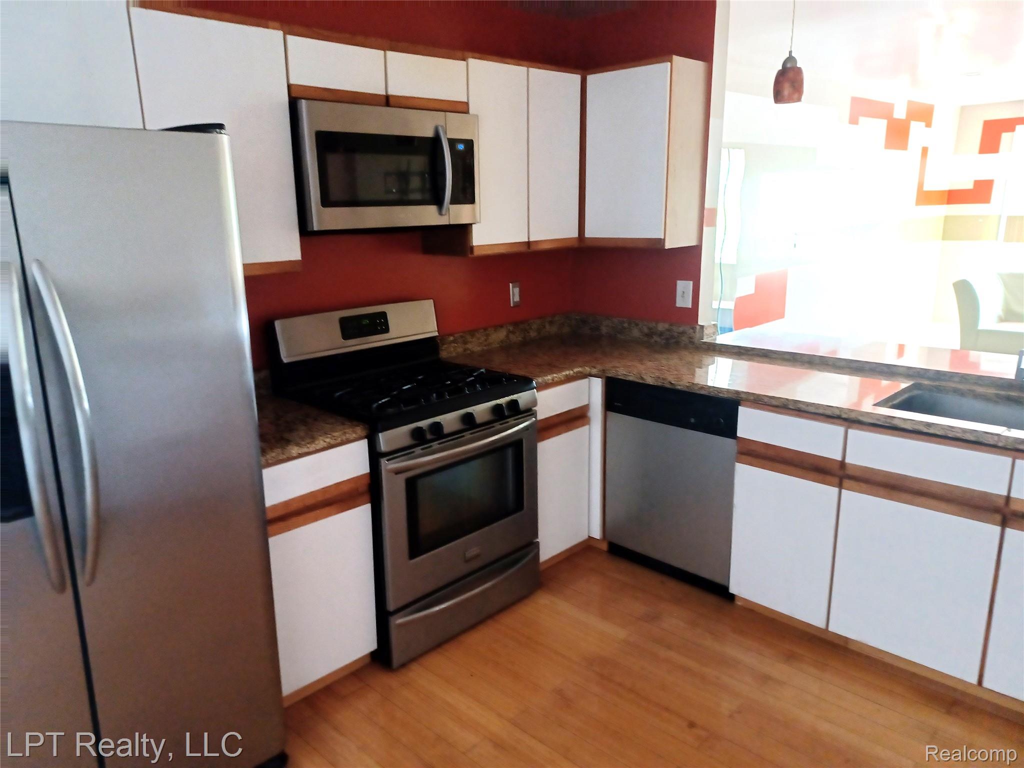 3304 Spinnaker Lane, Unit 47 Detroit, MI 48207 - Photo 10 of 21 Kitchen featuring stainless steel appliances, wood-finish flooring, granite countertops, white cabinetry, and a pass-through window