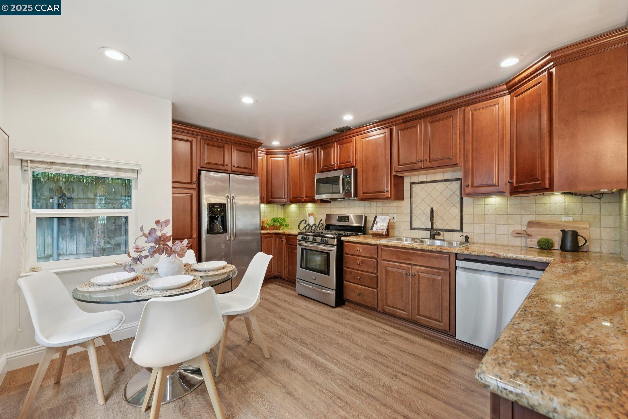 a kitchen with stainless steel appliances granite countertop a stove top oven a sink dishwasher a dining table and chairs with wooden floor