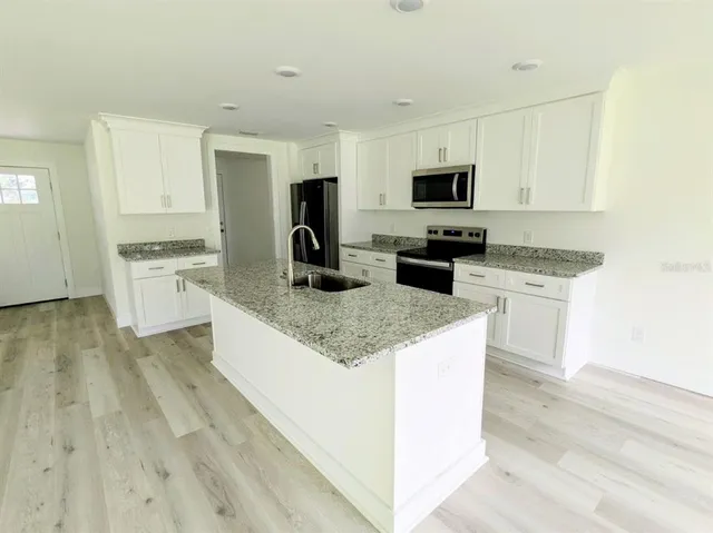 a kitchen with granite countertop a stove top oven a sink dishwasher and a refrigerator with wooden floor