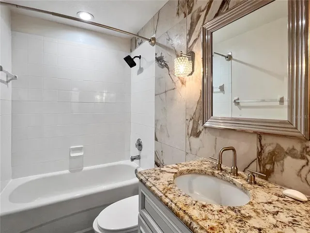 a bathroom with a granite countertop sink a toilet and bathtub