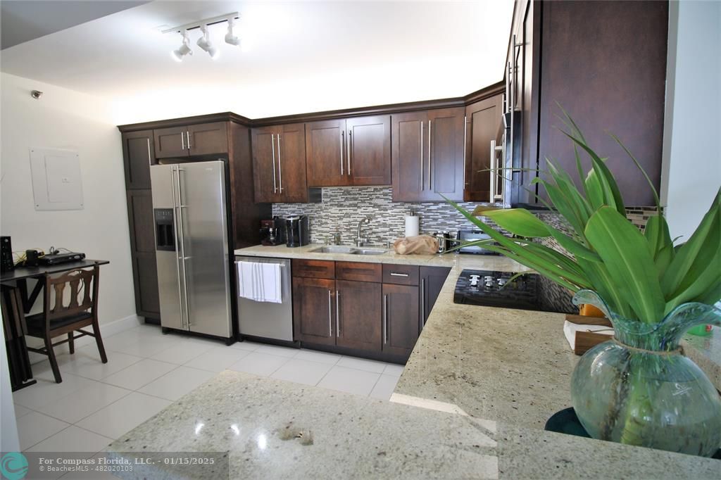 9341 Collins Avenue, Unit 1003 Surfside, FL 33154 - Photo 7 of 24 a kitchen with stainless steel appliances kitchen island granite countertop a refrigerator a stove and a wooden cabinets