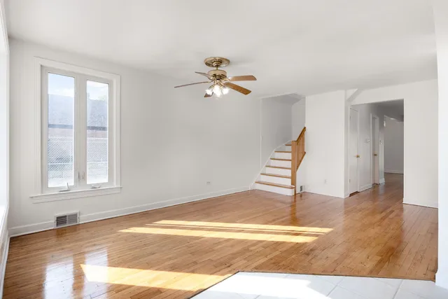 a view of an empty room with wooden floor and a ceiling fan