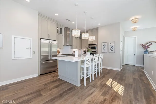 a kitchen with stainless steel appliances kitchen island granite countertop a refrigerator a stove a sink a dining table and chairs with wooden floor