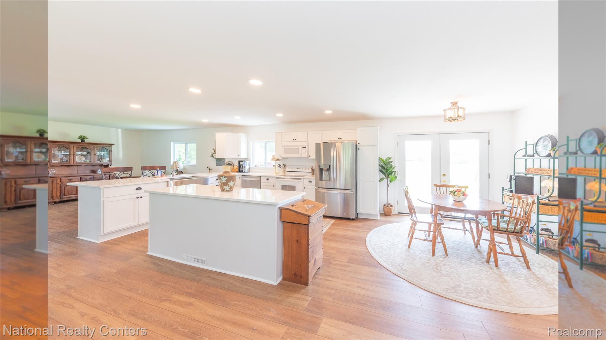 58191 8 Mile Road Northville, MI 48167 - Photo 35 of 57 Open-concept kitchen featuring white cabinetry, stainless steel appliances, two kitchen islands with solid surface countertops, wood-finish flooring, and recessed lighting