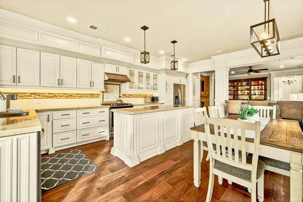 a kitchen with stainless steel appliances granite countertop a stove a sink dishwasher and white cabinets with wooden floor