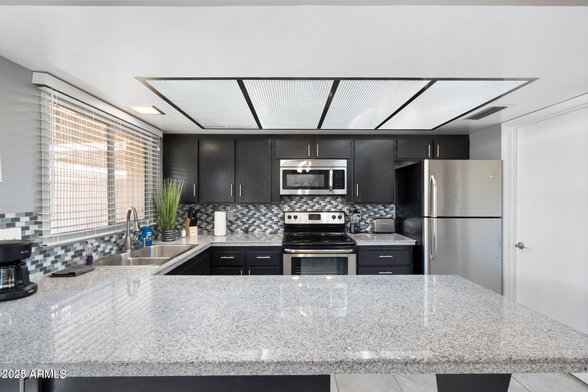 6921 East Osborn Road, Unit D Scottsdale, AZ 85251 - Photo 7 of 14 a kitchen with stainless steel appliances kitchen island granite countertop a stove a sink and a refrigerator