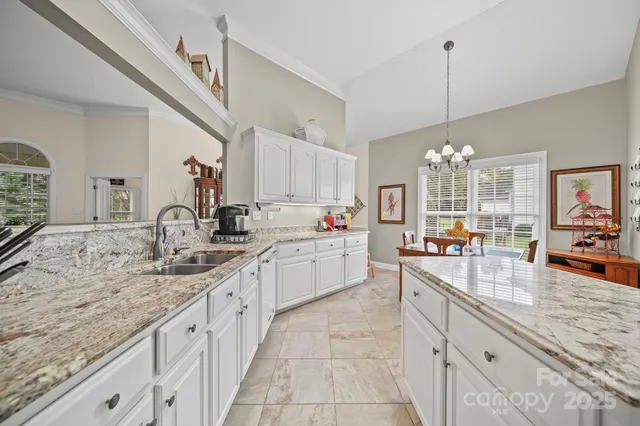 a large white kitchen with granite countertop a sink dishwasher a stove and white cabinets with wooden floor