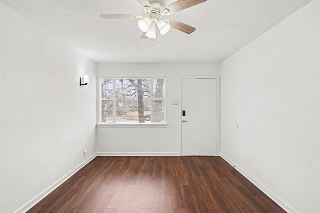 an empty room with wooden floor chandelier fan and windows