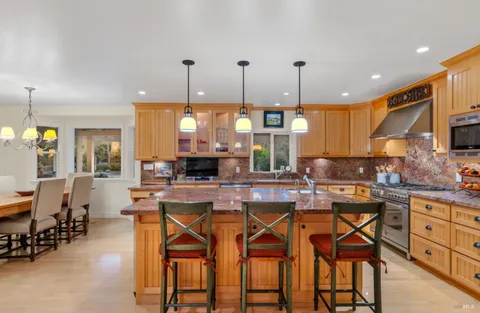a kitchen with stainless steel appliances kitchen island granite countertop a dining table chairs and white cabinets
