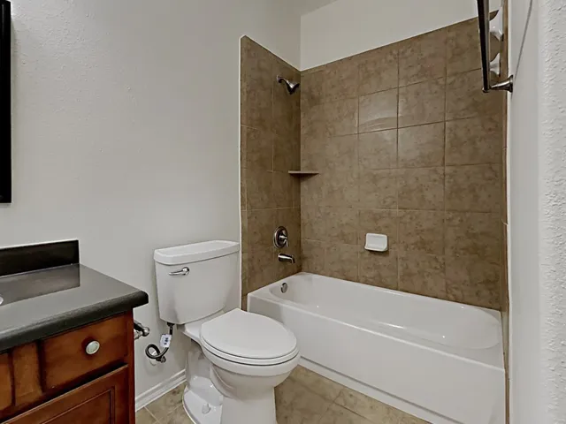 a bathroom with a granite countertop bathtub shower sink vanity and toilet