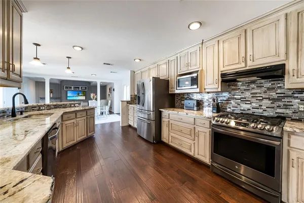 a kitchen with stainless steel appliances granite countertop a stove top oven a sink dishwasher and a refrigerator with wooden floor