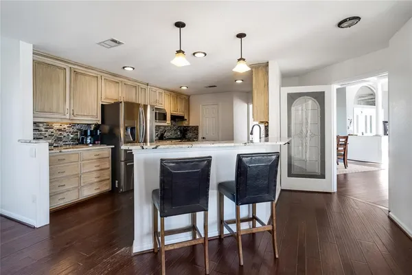 a kitchen with stainless steel appliances kitchen island granite countertop a refrigerator a stove top oven a sink dishwasher and white cabinets with wooden floor