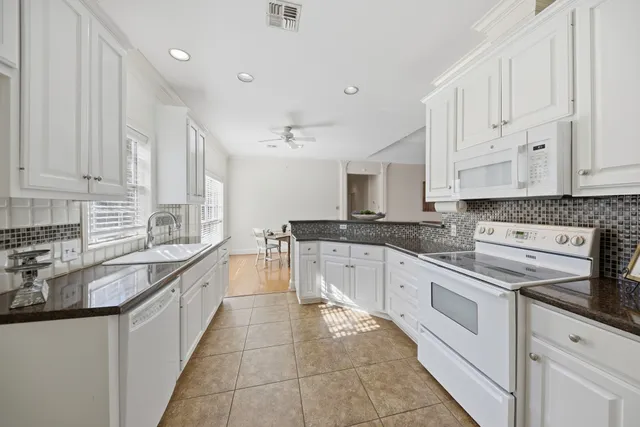 a large white kitchen with stainless steel appliances granite countertop a stove sink and cabinets