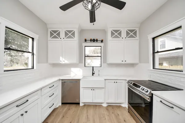 a large white kitchen with granite countertop a stove a sink dishwasher and a refrigerator with wooden floor