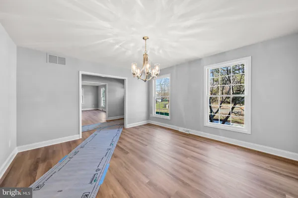 an empty room with wooden floor chandelier and windows