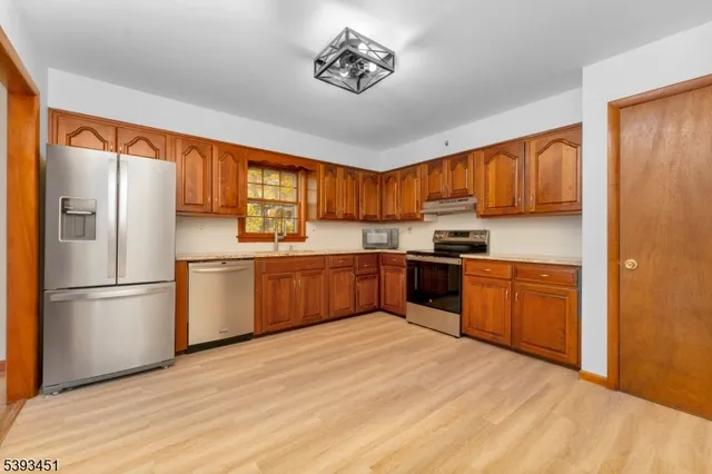 a kitchen with stainless steel appliances granite countertop a refrigerator sink and wooden cabinets