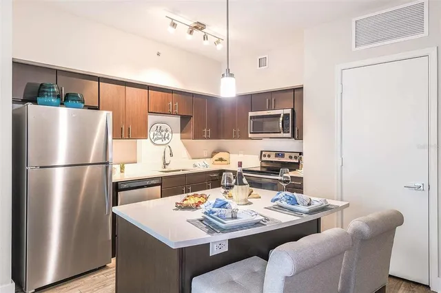 a kitchen with stainless steel appliances granite countertop a refrigerator a stove a sink a dining table and chairs with wooden floor