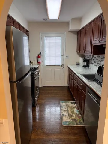 a kitchen with granite countertop a refrigerator a sink a stove white cabinetry and wooden floor