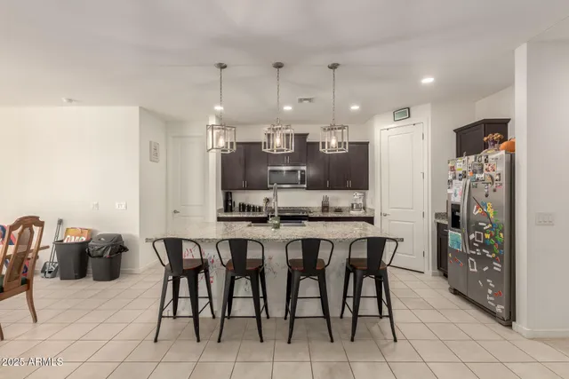 a kitchen with stainless steel appliances kitchen island granite countertop a dining table chairs and a refrigerator