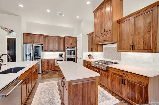 a kitchen with stainless steel appliances granite countertop a stove top oven a refrigerator a sink and dishwasher with wooden cabinets