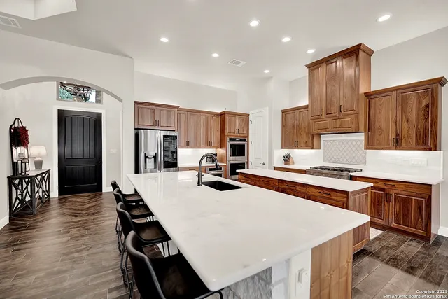 a kitchen with stainless steel appliances a stove top oven a sink dishwasher and a refrigerator with wooden floor