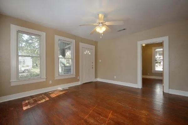 a view of an empty room with wooden floor and a window