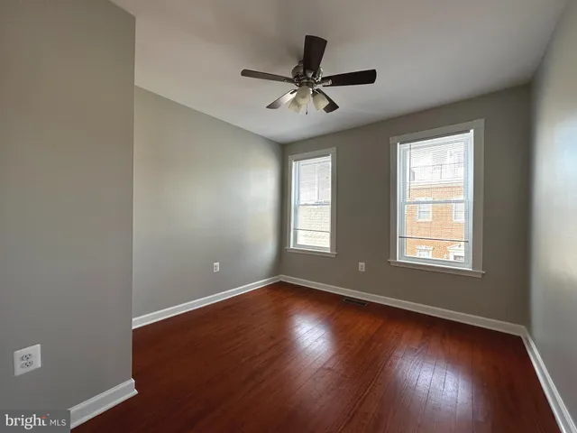 an empty room with wooden floor fan and windows