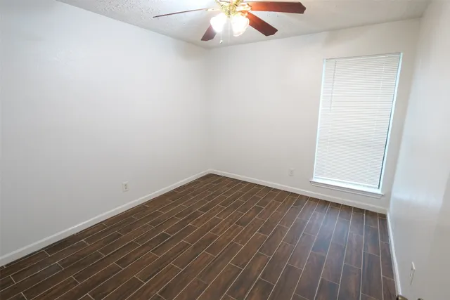 a view of an empty room with wooden floor and a chandelier fan