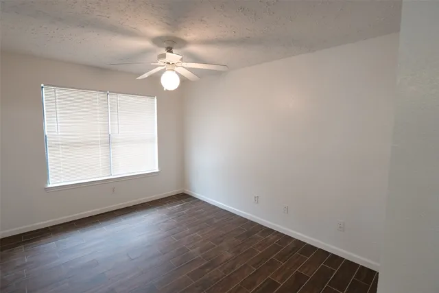 an empty room with wooden floor fan and windows