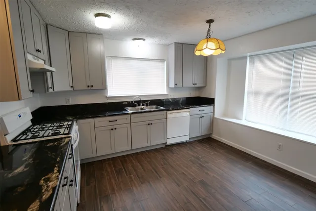a kitchen with granite countertop a stove a sink a cabinets and wooden floor