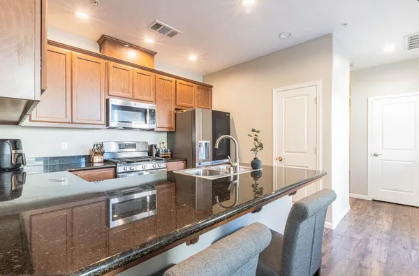 a kitchen with stainless steel appliances granite countertop a stove top oven a sink dishwasher a dining table and chairs with wooden floor