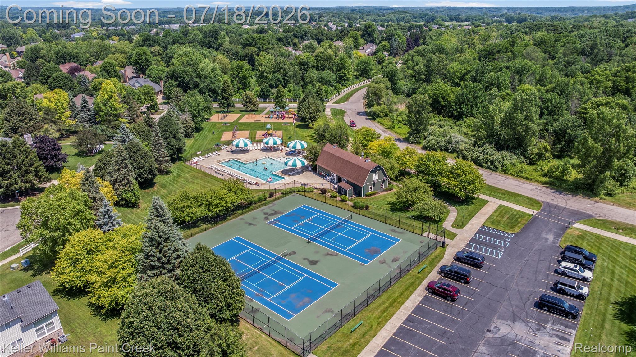 4230 Holly Lane Rochester, MI 48306 - Photo 62 of 64 Dual tennis courts with fencing, a swimming pool with covered seating, and an adjacent recreational building, surrounded by mature trees and residential areas