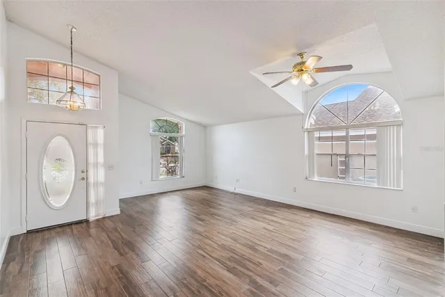 an empty room with wooden floor chandelier fan and windows