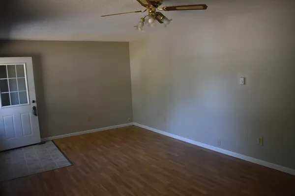an empty room with wooden floor fan and windows
