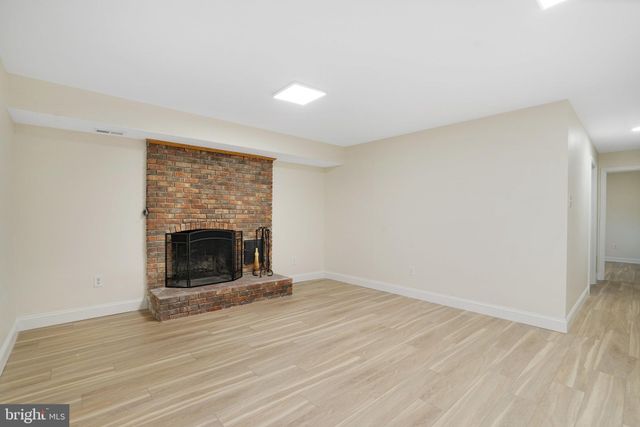 a view of an empty room with wooden floor fireplace and a window