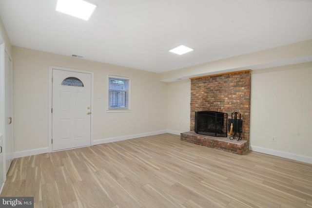 a view of an empty room with wooden floor fireplace and a window