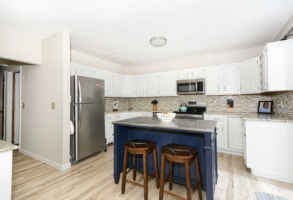 307 Ridgefield Circle, Unit C Clinton, MA 01510 - Photo 4 of 18 a kitchen with stainless steel appliances a refrigerator a stove a sink dishwasher and white cabinets with wooden floor