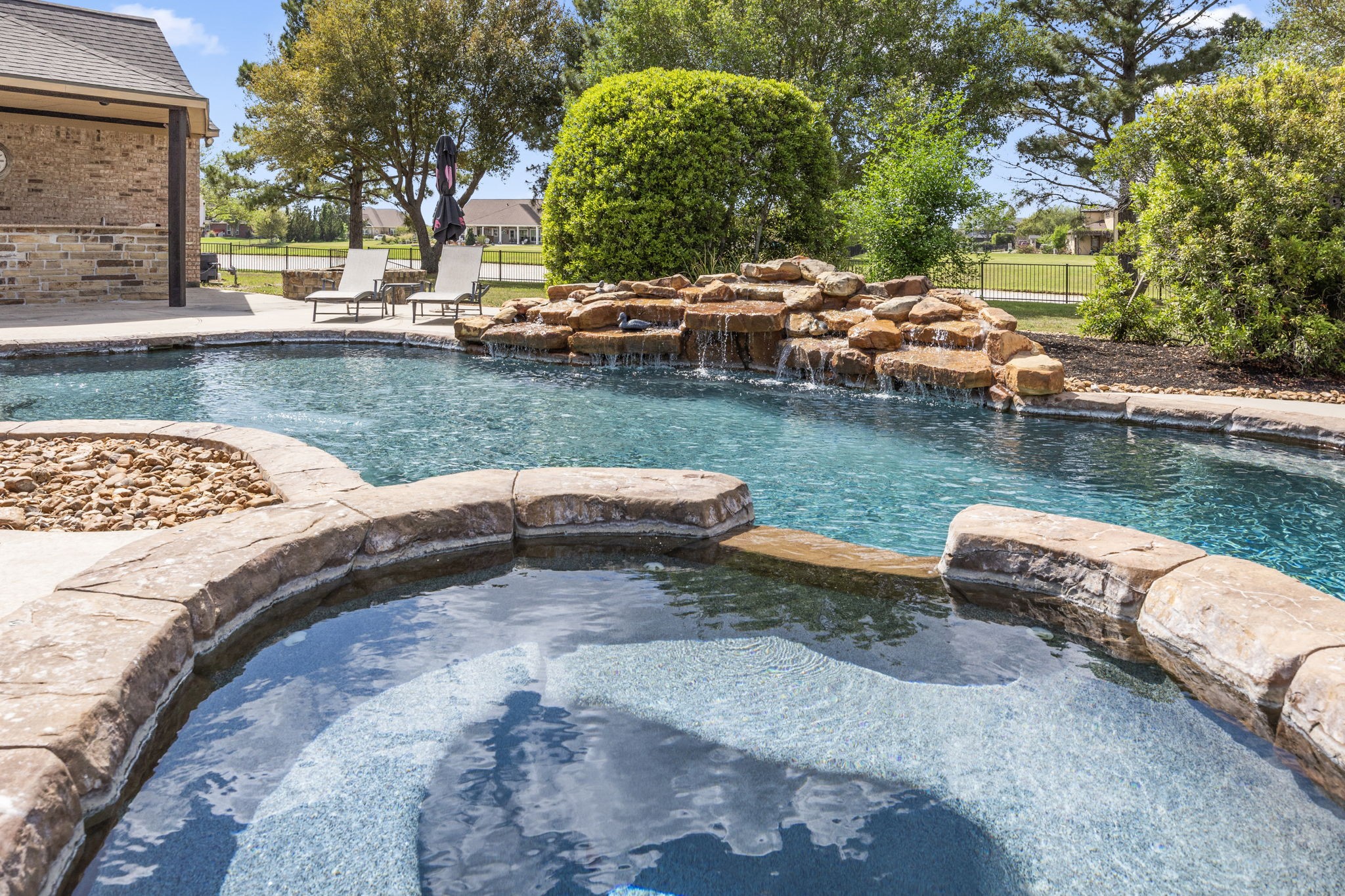 4611 Oasis Point Katy, TX 77493 - Photo 4 of 41 Enjoy the lake views beyond the stone waterfall from your spa. Pebbletech pool surface maintains the blue visual impact of the water year round. A custom fitted Catch-a-Kid system conveys with the pool.