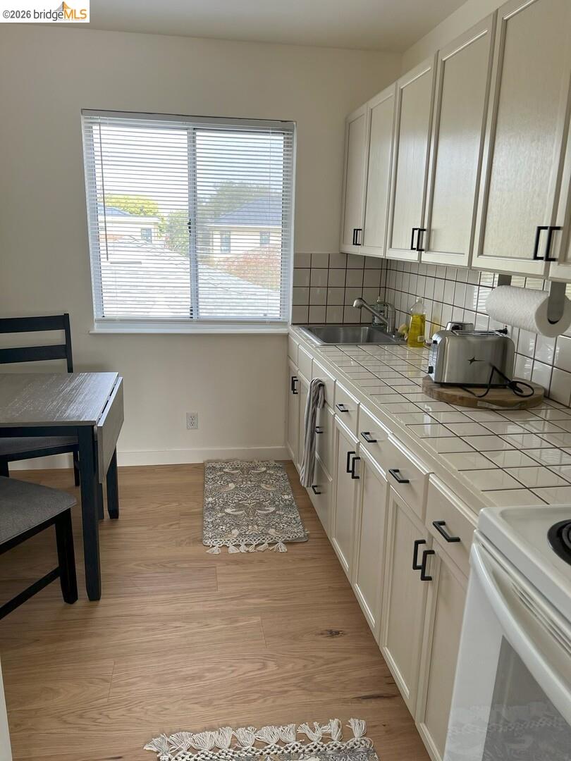 1728 Seventh Street, Unit F Berkeley, CA 94710 - Photo 5 of 6 kitchen with white range with electric stovetop, backsplash, white cabinets, light wood finished floors, and tile countertops