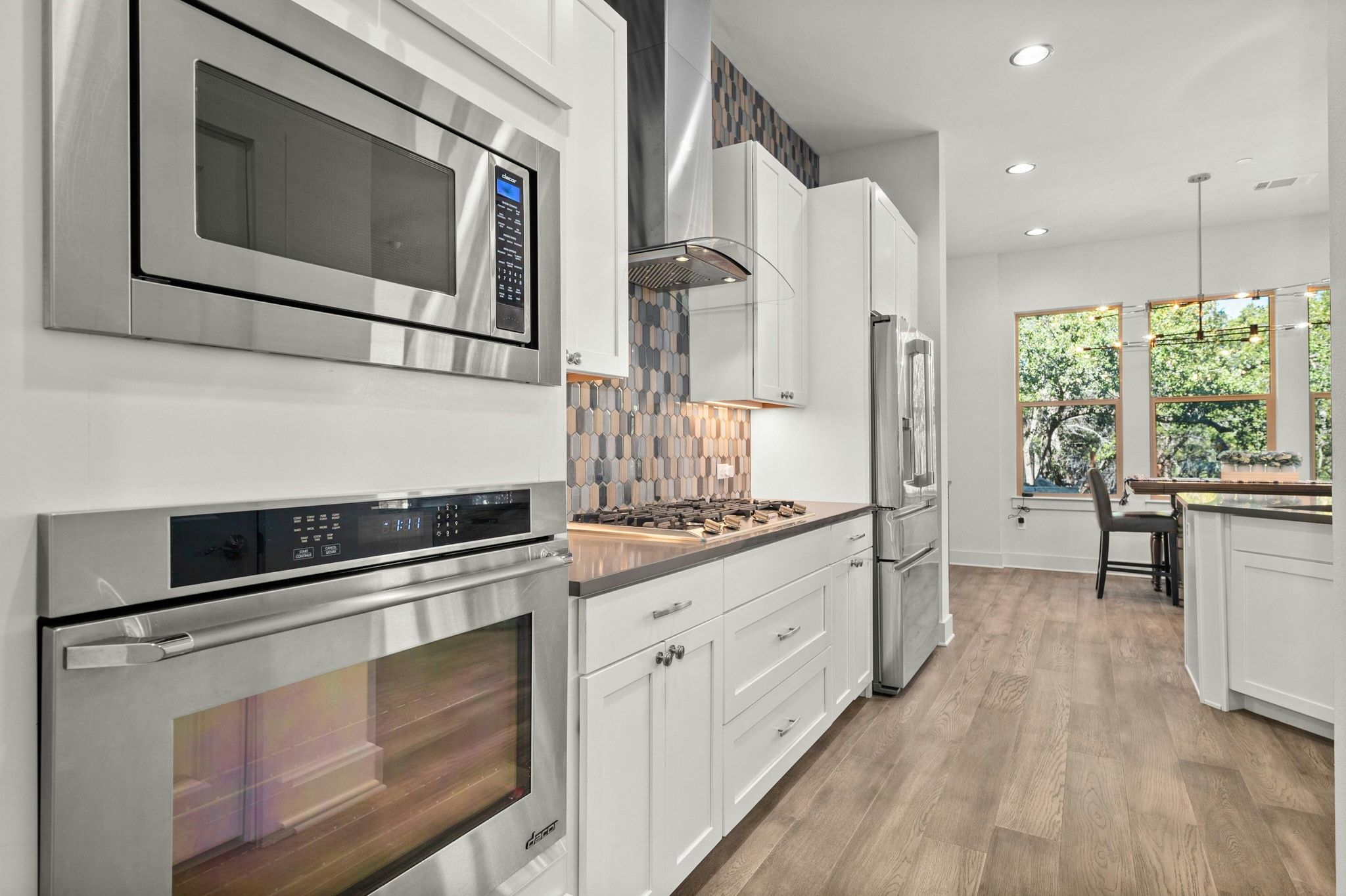 8110 Ranch Road 2222, Unit 92 Austin, TX 78730 - Photo 9 of 40 Kitchen featuring stainless steel appliances, white cabinetry, wood-finish flooring, a mosaic tile backsplash, and recessed lighting