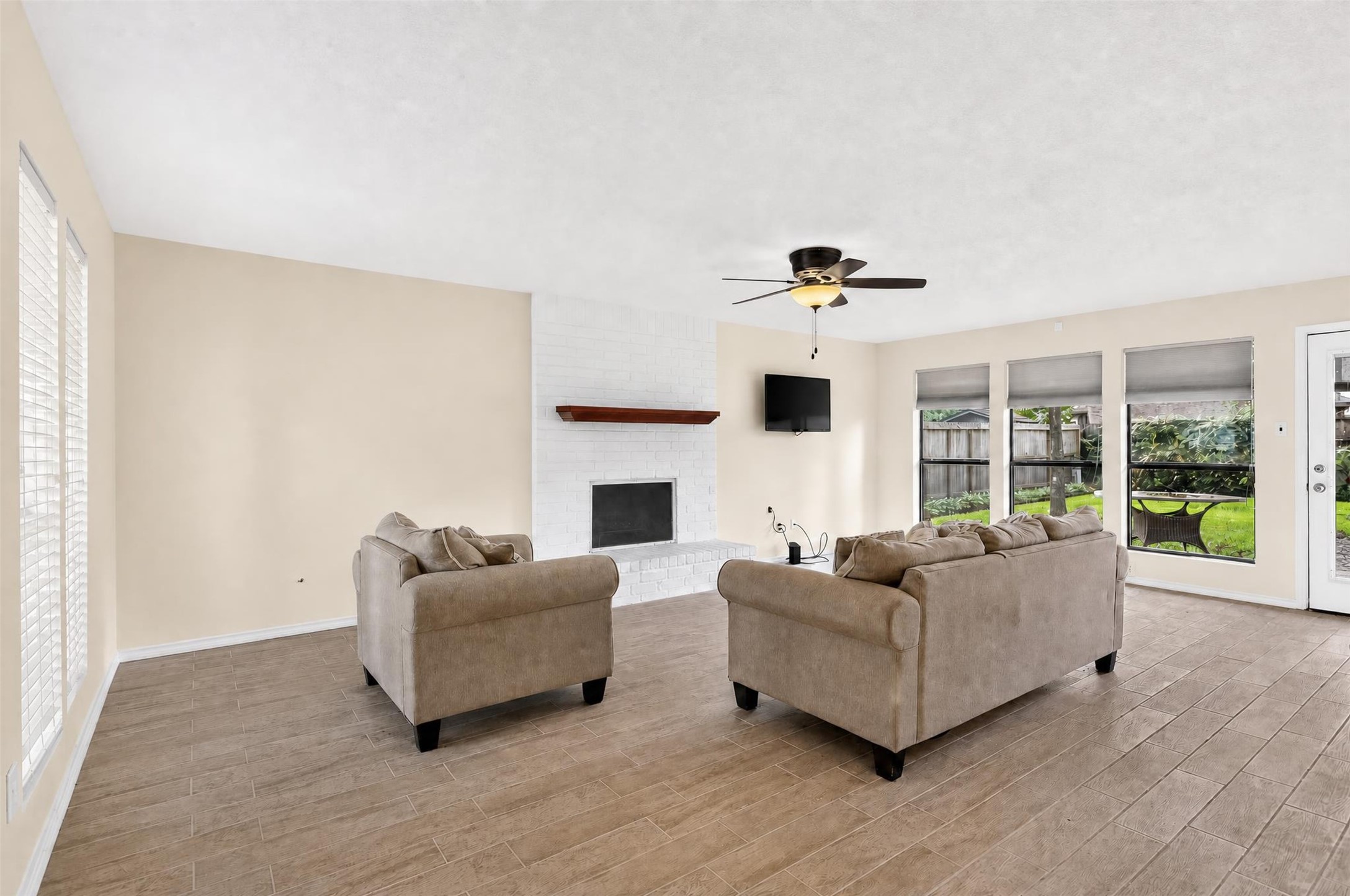 7019 Wyoma Trail Spring, TX 77379 - Photo 3 of 34 Spacious living room with a cozy brick fireplace, abundant natural light, and a view of the lush backyard through large windows.