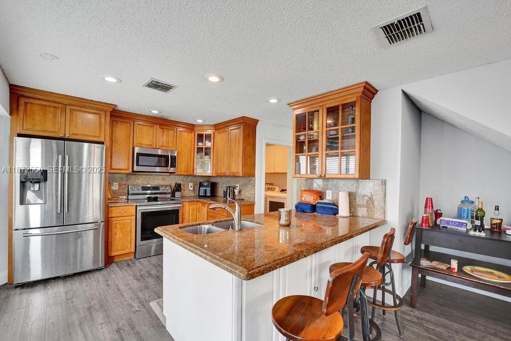 2747 Pinewood Court Davie, FL 33328 - Photo 12 of 25 a kitchen with stainless steel appliances granite countertop a stove a refrigerator a sink a dining table and chairs with wooden floor