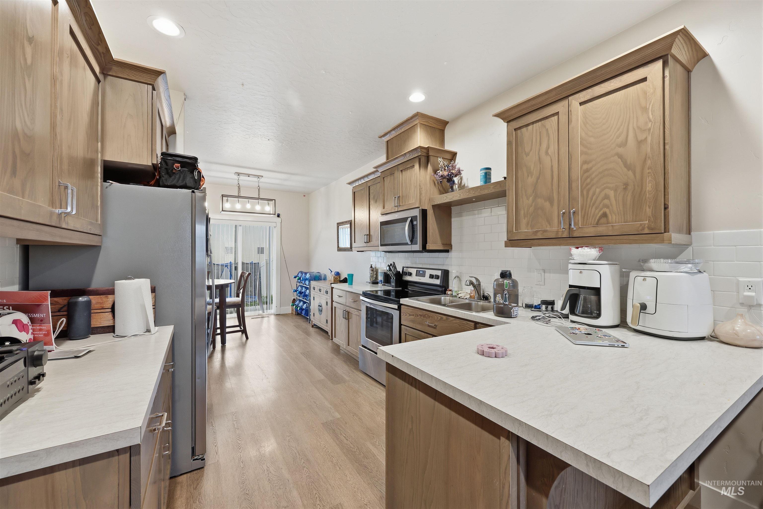 6341 South Ruddsdale Avenue Boise, ID 83709 - Photo 6 of 41 Kitchen with appliances with stainless steel finishes, a peninsula, light countertops, hanging light fixtures, and light wood-style flooring